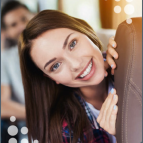 Eine junge Frau mit dunklen, langen Haaren blickt seitlich an einem Sitz im Bus vorbei und lächelt freundlich.