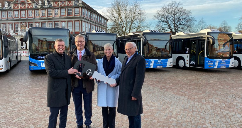 Drei Mitarbeiter und eine Mitarbeiterin der Unternehmen KVG und MAN stehen in Wolfenbüttel vor den neuen Gelenkbussen, halten einen großen Schlüssel mit dem MAN-Logo in den Händen und lächeln in die Kamera.