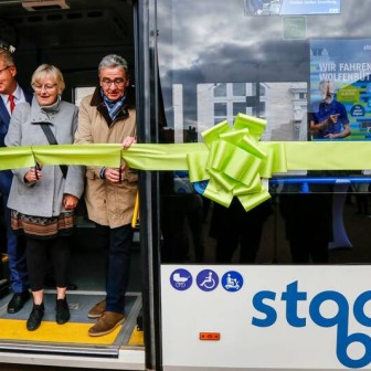 Axel Gierga (KVG), Susanne Koch (RGB) und Thomas Pink (Bürgermeister Wolfenbüttel) schneiden feierlich ein hellgrünes Eröffnungsband, das um den neuen Stadtbus in Wolfenbüttel gewickelt wurde, durch.