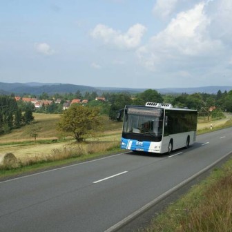 Ein Bus der KVG Braunschweig fährt bei bewölktem Himmel über eine Landstraße. Im Hintergrund ist das Panorama des Harz-Gebirges erkennbar.