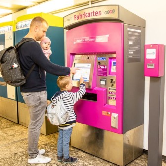 Ein Vater zeigt seinen Kindern, wie man ein Ticket am Automaten kauft.