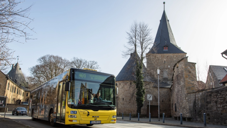 Ein gelber Bus der Linie 801 von Stadtbus Goslar fährt durch Goslar. Im Hintergrund steht eine Kirche.