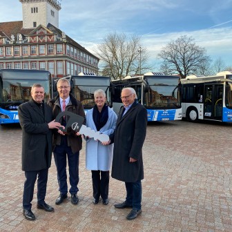 Drei Mitarbeiter und eine Mitarbeiterin der Unternehmen KVG und MAN stehen in Wolfenbüttel vor den neuen Gelenkbussen, halten einen großen Schlüssel mit dem MAN-Logo in den Händen und lächeln in die Kamera.