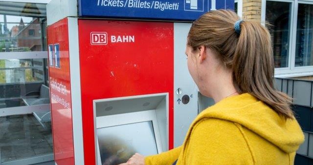 Eine Frau in einem gelben Pulli kauft an einem Automaten der Deutschen Bahn ein VRB-Ticket.