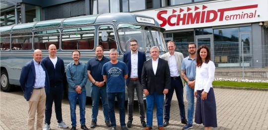 Einige Mitarbeiter der Verkehrsunternehmen Evakon, VLG Gifhorn, WVG, Stadtbus Goslar, Mundstock, Der Schmidt, Blic und ONS stehen vor einem alten Busmodell am SchmidtTerminal in Wolfenbüttel und lächeln in die Kamera.